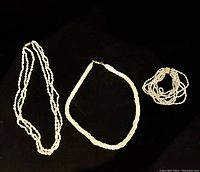 Image showing the two freshwater pearl necklaces and one multi-strand freshwater pearl bracelet laid flat on a black background, highlighting their overall look and size.
