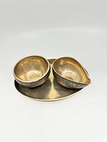 Top view of two bronze bowls with ornate exterior engravings sitting on a bronze oval tray.