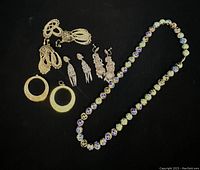 Overview of all jewelry items including four pairs of silver earrings and a cloisonné bead necklace on black background.