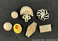 Photo showing the full lot of seven vintage brooches arranged together on a black background for clear view of designs and colors.