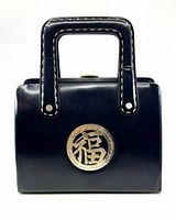 Front view of the vintage black leather purse showing the gold-tone Asian character medallion and black handles with white stitching.