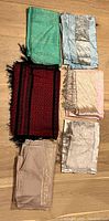Group of 7 scarves in various colors arranged on a wooden floor showing different textures and fringes.