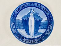 Front view of a 1919 Royal Copenhagen commemorative plate showing a woman in blue and white robes standing in a landscape, bordered by decorative blue text and symbols.
