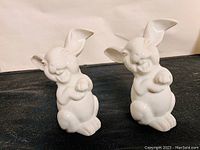 Two white porcelain laughing rabbit figurines facing forward showing their detailed facial expressions and posture.