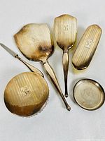 Photo of the full set showing five monogrammed sterling silver dresser items including mirror, brushes, comb, and dish
