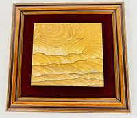 Front view of framed golden sandstone slab with natural wave-like pattern and gold-tone wooden frame.