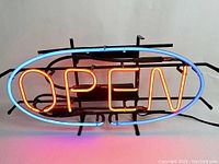 Front lit view of neon OPEN sign showing red letters 'OPEN' inside a blue oval border, stand attached.