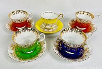 Five bone china cups and saucers, four Royal Albert and one Sutherland, showing front view with colors red, orange, green, blue, and yellow, displayed on white background.