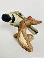 Front-side view showing the chickadee's head and the ladybug on the branch base