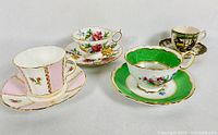 Photo showing four vintage bone china cups and saucers with varied designs and colors, indicating condition and detailing.