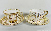Photo of two hand decorated bone china cups and saucers, one with gold wheat motif, the other with peacock feather motif in gold, blue and brown.
