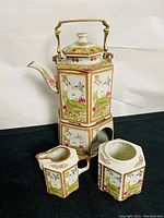 Front view of hexagonal porcelain teapot with brass handle, warmer, creamer and strainer with detailed floral and bird artwork