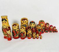 Full set of 19 wooden Matryoshka nesting dolls arranged in line by size, showing colorful folk-art style hand-painted designs.