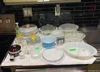 Overview of all items on a white cloth including plates, bakeware, egg cups, vintage bottle, and Pyrex/Glassbake dishes.