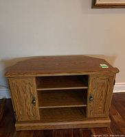 Front view of oak colored media cabinet with open central shelves and two closed side doors with metal handles.