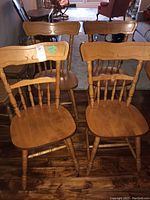 Photo showing the four wooden dining chairs grouped together on a wooden floor with a living room setting in background.