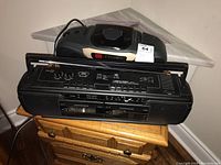Photo showing Realistic SCR-38 radio and cassette player and Koss PC-35 radio and CD player stacked on small wooden side table near a fireplace.