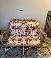 Frontal view of the vintage rattan loveseat showing cushion pattern and overall shape.