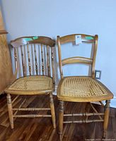 Front view of two wood-framed vintage chairs with woven rattan seats, one with curved backrest and one with spindle backrest.