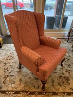 Side view of the wing chair showing brocade fabric upholstery, winged backrest, and wooden cabriole legs.