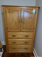 Front view of the Shermag tallboy dresser showing two cabinet doors with brass handles above three drawers with brass pulls, natural oak finish.