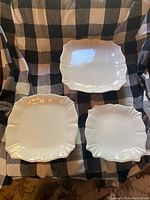 Three white ceramic stackable serving plates with scalloped edges laid out on a black and white checkered cloth.