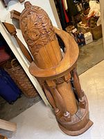 Full view of the heavily carved oak newel post with attached spindles seen leaning against a wall in storage.
