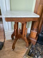 Side view of antique walnut side table showing marble top and carved base with casters.