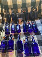 Eighteen blue glass beverage bottles arranged on a checkered cloth, with a small sealed package of replacement rubber gaskets in the center.