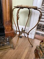 Full view of Victorian metal plant stand showing marble top and curved metal legs.