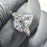 Close-up view of pear cut clear gemstone and prong setting in 14K white gold ring.