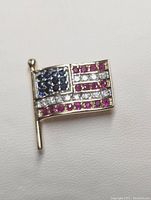 Front view of 14K yellow gold American flag pin with pavé gemstones in red rubies, blue sapphires, and white diamonds.