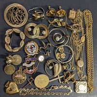 Collection of various gold filled jewelry pieces arranged on a black background showing pins, earrings, lockets, and necklaces.
