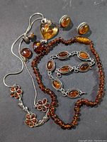 Photo showing assorted amber jewelry including bead necklaces, pendants, earrings, and a bracelet on a dark surface.