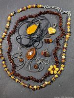 Full view of the amber jewelry lot showing necklaces, pendants, earrings spread on a flat surface including multi-colored amber bead necklace and a dark amber bead necklace, several pendants in amber and sterling silver, and amber earrings.