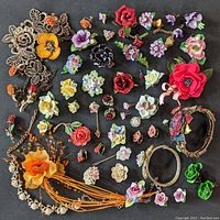Overview of assorted bone china floral brooches, earrings, and floral motif jewelry laid out on black background showing multiple flower designs in various materials and colors.