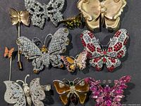 Top view showing eleven assorted butterfly brooches with various colors, rhinestones, pearls, metal and enamel materials.