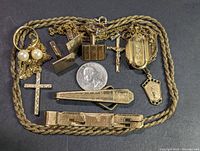 Photo showing all items laid flat including crosses, cufflinks, chain, tie clips, and medallion with a quarter for scale