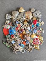 Image showing a large assortment of heart-shaped pendants and jewelry pieces in various materials and colors spread out on a grey surface.