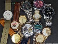 Collection of 11 men's wristwatches arranged together showing variety of dials, straps and bracelets.