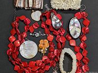 Variety of mother of pearl jewelry laid out on dark background including necklace strands, pendants, earrings, bracelets, and small pins.