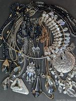 Assorted statement necklaces with large faceted glass and crystal prism pendants, laid out on dark surface showing variety of styles and bead types.
