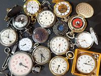 Overview photo of assorted pocket watches and stopwatches showing various sizes, colored metal cases, and dial styles including Arabic and Roman numerals and stopwatch dials.