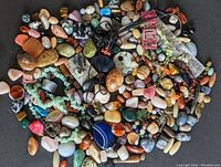 Top view of a large assortment of polished semi precious rocks and stones in various colors, shapes and sizes, including some beads and pendant bails