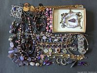 Overview of assorted purple tone costume jewelry including various necklaces, bracelets, earrings, and pendants arranged on a flat surface.