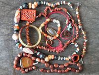 Photo showing assorted red agate jewelry including carved bangle, carved rectangular ring, irregular beads, and polished round bead necklaces with pendants.