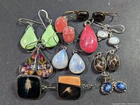 Top-down shot showing 9 pairs of sterling silver earrings with various stones and a pendant on a dark surface.