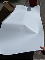 Person holding a large white flexible plastic sheet to show size and flexibility.