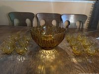 Amber glass punch bowl with 12 matching cups arranged around it on a wooden table.