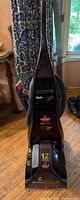Front view of the upright Bissell ProHeat carpet cleaner showing black body and handle with attached suction hose.
